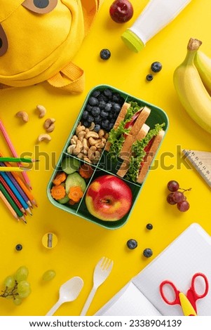 Elevate school meal experience - vertical top view of lunchbox filled with nutritious bites, cutlery, yogurt, stationery, color pencils, copybook, scissors, funny schoolbag on yellow backdrop Royalty-Free Stock Photo #2338904139