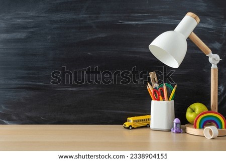 Enhance your study sessions with this student's workplace. Side view photo featuring desk lamp, stationary and toys on wooden table on blackboard isolated background, perfect for promotional messages