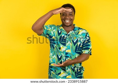 Young latin man wearing hawaiian shirt over yellow background gesturing with hands showing big and large size sign, measure symbol. Smiling looking at the camera.