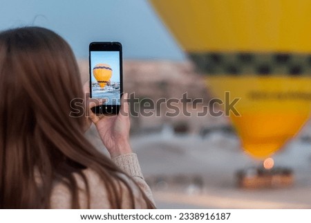 Girl taking photos of the launch hot air balloon using the phone. Close-up shot of the hand holding the phone with the fire of the hot air balloon behind. Goreme national park of Сappadocia.  Royalty-Free Stock Photo #2338916187