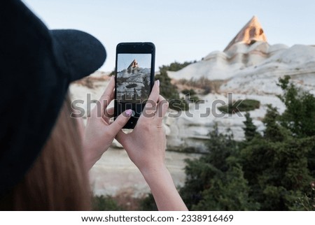 Girl taking photos of the cave temple using the phone. Close-up shot of the hand holding the phone with the mountain behind. Goreme national park of cappadocia. 