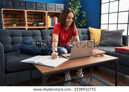 Young beautiful hispanic woman student writing on notebook studying at home