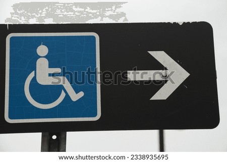 handicap sign blue logo with white arrow on its right pointing right on black rectangle horizontal sign on post with sky in background, space on right.