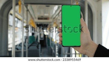 Woman Hand is holding a Smartphone with Green Screen in Vertical Position. Empty modern Bus, Tram, Public Transport on Background, Quarantine. Apps. Technology. Phones.