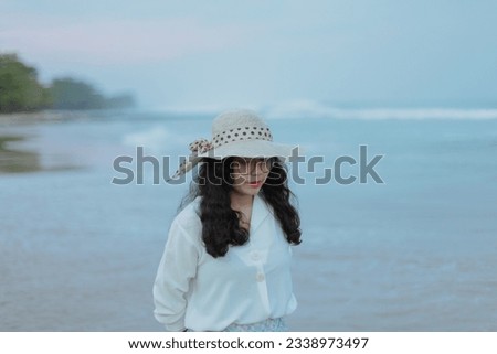 An Asian woman wearing glasses and a floppy hat is walking on the beach, taking a stroll and enjoying the refreshing atmosphere of the beach and blue sea. beach background