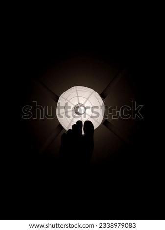 A white balcony chandelier with a light bulb against the black background of the room and a picture of a black foot