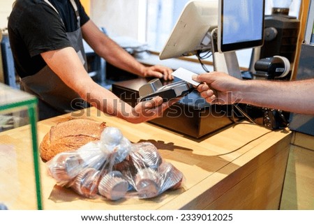 An unidentified worker's hands in a bakery, using a card reader to accept payment for muffins and a loaf of bread