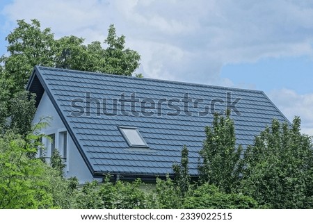 attic of a private house under a gray tiled roof with one window among green trees and vegetation on the street against the background of the sky and clouds Royalty-Free Stock Photo #2339022515