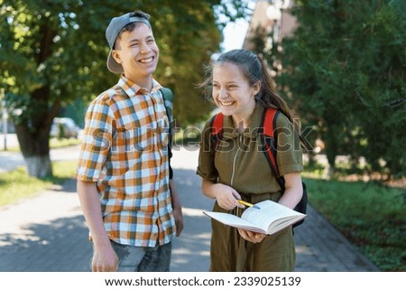 school students, a teenage boy and a girl are walking down the street, having fun, talking, reading books, a bright summer day in a city park Royalty-Free Stock Photo #2339025139