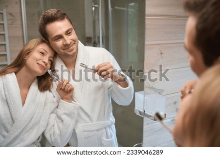 Young male and female brush teeth in bathroom, looking in mirror