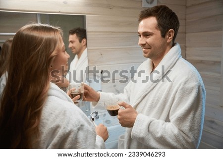 Man giving coffee to woman while standing near bathroom mirror