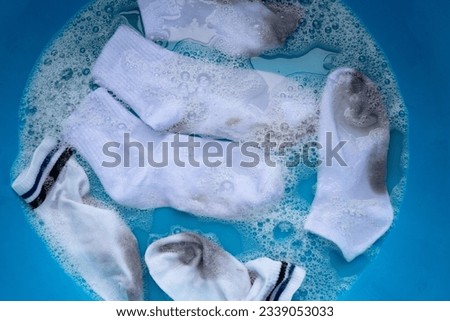 Dirty white socks soaked in water, dissolving detergent in blue basin.