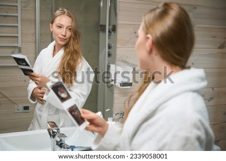 Woman looking in mirror holding pregnancy ultrasound photo