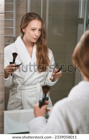 Woman looks at herself in the mirror and holds brushes