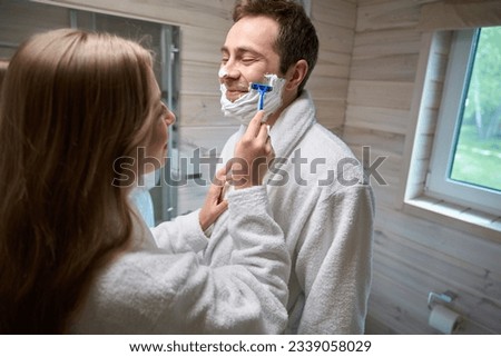 Man and woman standing in bathtub woman shaving man face