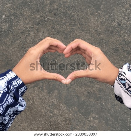 two women's hands forming a heart against a background of worn asphalt ground.  This photo was taken when it started to rain in the parking lot