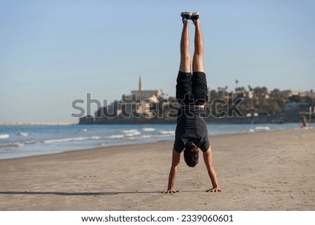 Young man doing yoga exercise - handstand on sandy beach near the sea. Active lifestyle concept.