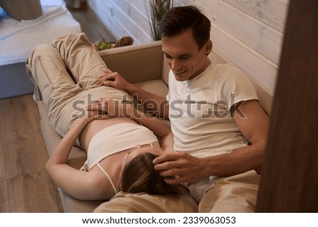 Woman is lying on a sofa in a room, a man is stroking a woman