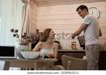 Couple in the kitchen, a man makes tea, a woman cuts a cucumber