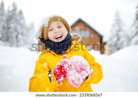 Happy preteen boy having fun playing with fresh snow during snowfall in european Alps. Child dressed in warm clothes, hat, hand gloves and scarf. Active winter outdoors leisure for children
