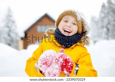 Preteen boy having fun playing with fresh snow during vacation in european Alps. Child dressed in warm clothes, hat, hand gloves and scarf. Active winter outdoors leisure for kids on holidays time