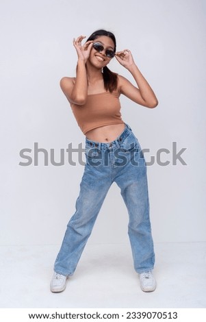 A confident Filipino woman in her late teens or early 20s. Wearing a brown top and loose fitting jeans. Isolated on a white backdrop. Royalty-Free Stock Photo #2339070513