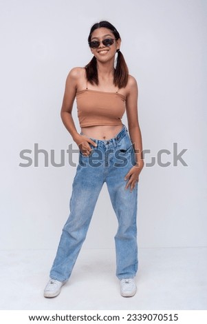 A confident Filipino woman in her late teens or early 20s. Wearing a brown top and loose fitting jeans. Isolated on a white backdrop. Royalty-Free Stock Photo #2339070515