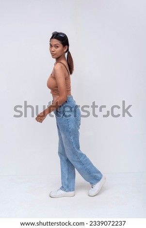 A young FIlipino woman taking a walk while looking at the camera. Side view and Full body photo, isolated on a white background. Royalty-Free Stock Photo #2339072237