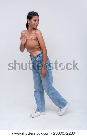 A young FIlipino woman walking looks back with a pleasant reaction. Full body photo, isolated on a white background.
