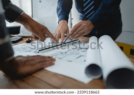 Team of engineers reviewing blueprints Sketch of a new construction project with engineering tools at office desk. For improvement of house designs in mortgage, rent, sale, real estate Royalty-Free Stock Photo #2339118663