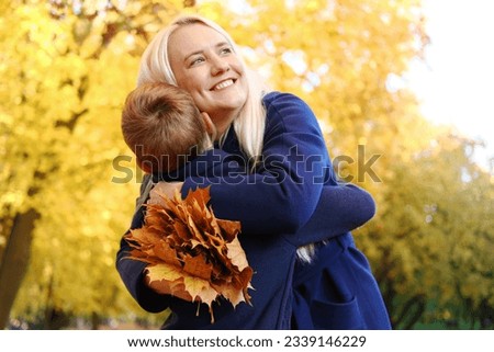 The boy gave his mother a bouquet of autumn leaves and his mother hugs him. Horizontal photo