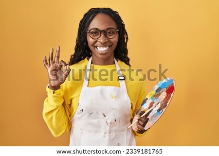 African woman holding painter palette smiling positive doing ok sign with hand and fingers. successful expression. 