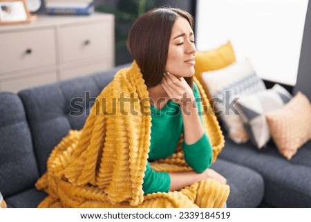 Young beautiful hispanic woman suffering for throat pain sitting on sofa at home Royalty-Free Stock Photo #2339184519