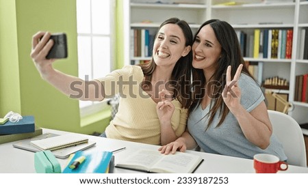 Two women sitting on table studying make selfie by smartphone at library university