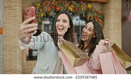 Two women going shopping holding bags make selfie by smartphone at street