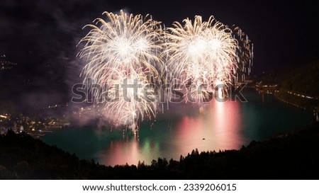 Long exposure fireworks celebration festival days reflecting in the lake with different vibrant colours with from above , during night in austria, mountain near klopeiner see lake