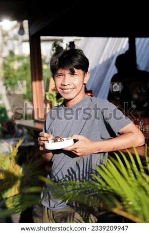 Happy Asian man in cafe with plate of brownies in hand