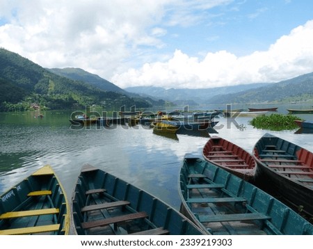 Colourful bright blue rowing boats on tranquil Phewa Lake, Pokhara, Nepal with clouds reflected in water and mountains in the background. High quality photo