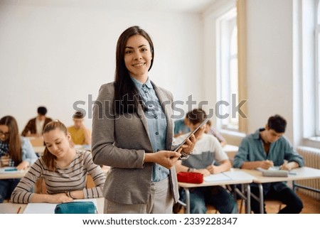 Happy high school teacher in the classroom looking at camera while her students are learning int he background.