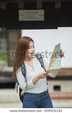 A young female college student who is looking for her way while looking at a map with a backpack in a traditional Korean village