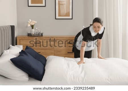 Young chambermaid making bed in hotel room