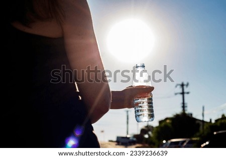 Bottle with water in a woman's hand against bright sun outdoors. Climate change hotness concept 
