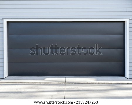 Double gray garage with black tilt-up retractable raised panel metal door