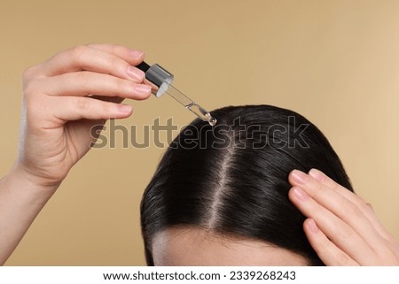 Woman applying essential oil onto hair roots on beige background, closeup Royalty-Free Stock Photo #2339268243