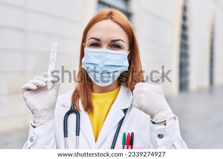 Young doctor woman holding coronavirus infection test smiling happy and positive, thumb up doing excellent and approval sign 