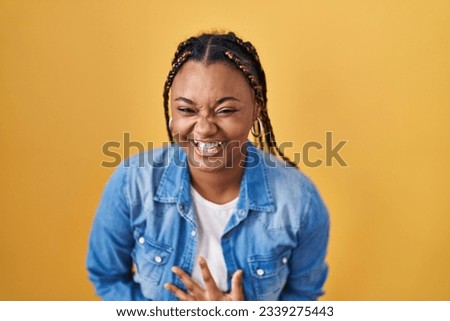 African american woman with braids standing over yellow background smiling and laughing hard out loud because funny crazy joke with hands on body.  Royalty-Free Stock Photo #2339275443