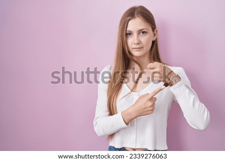 Young caucasian woman standing over pink background in hurry pointing to watch time, impatience, looking at the camera with relaxed expression 