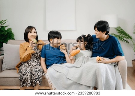 Asian Overjoyed kids sitting on sofa with cheerful parents, watching funny video on computer. Happy married couple enjoying spending weekend time with children, looking at laptop and tablet  Royalty-Free Stock Photo #2339280983