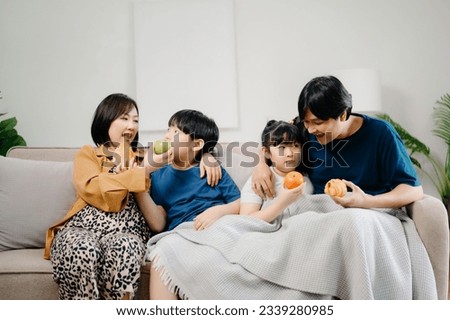 Asian Overjoyed kids sitting on sofa with cheerful parents, watching funny video on computer. Happy married couple enjoying spending weekend time with children, looking at laptop and tablet  Royalty-Free Stock Photo #2339280985