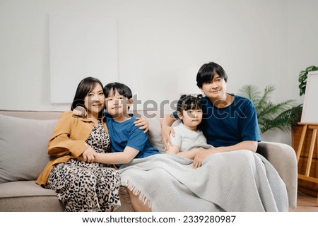 Asian Overjoyed kids sitting on sofa with cheerful parents, watching funny video on computer. Happy married couple enjoying spending weekend time with children, looking at laptop and tablet  Royalty-Free Stock Photo #2339280987
